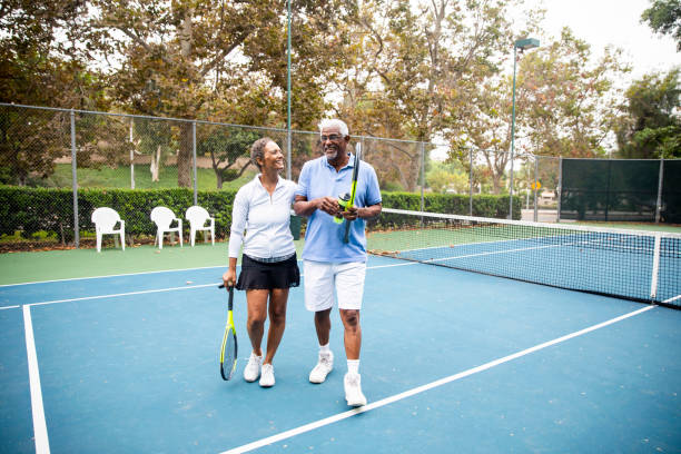 senior black couple walking off the tennis court - tennis active seniors healthy lifestyle senior men imagens e fotografias de stock