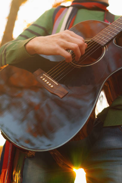 istock Young blond man playing acoustic guitar under a tree in autumn. 1058174022