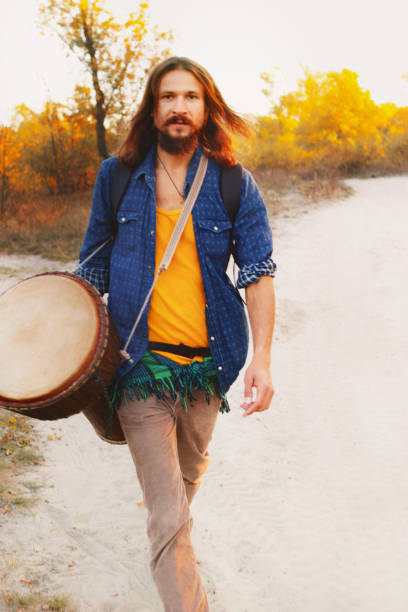 Hippie man playing djembe drum in autumn forest.