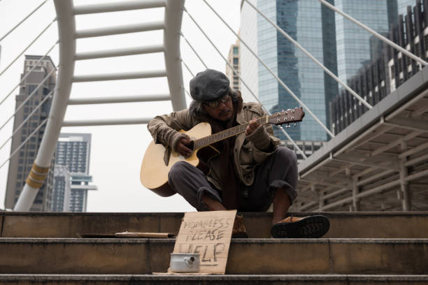 istock Old beggar play guitar in city to get donate 1058174108