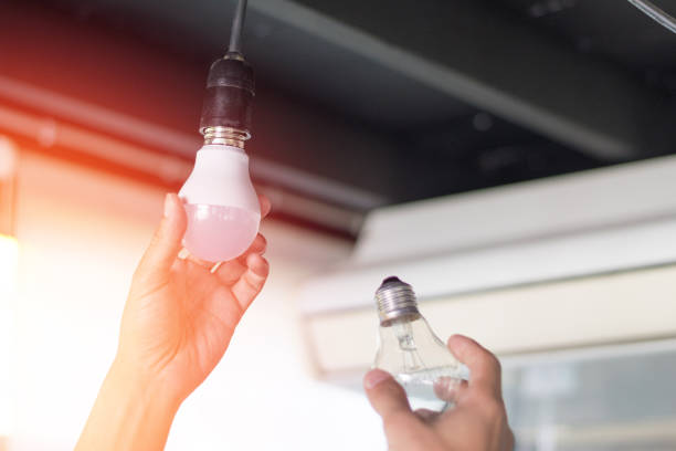 istock Power saving concept. Asia man changing compact-fluorescent (CFL) bulbs with new LED light bulb. 1058192816