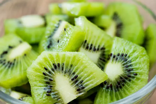 A bowl of kiwi fruit slices on wooden table.