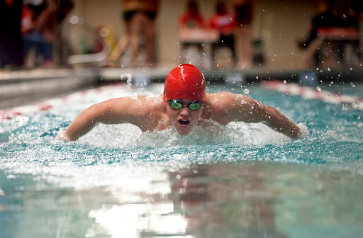Young man swimming butterfly stroke for high school varsity sports. (Fast action, low light, selective focus)