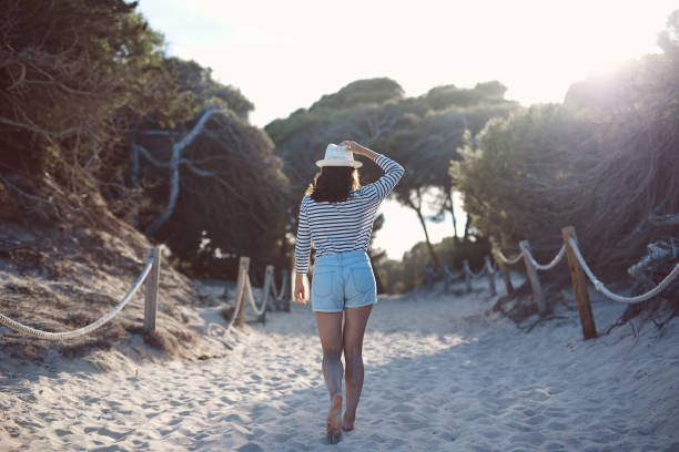 istock Rear view of young woman walking on sandy footpath 1058199948