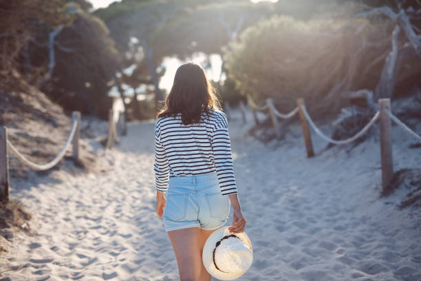 istock Rear view of young woman walking on sandy footpath 1058200974
