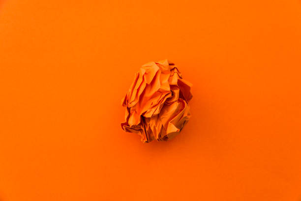 Orange crumpled paper ball on orange background.