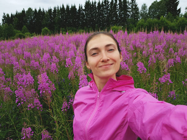 A girl in a purple sports jacket makes a selfie in a beautiful bright field of Ivan-tea during flowering. Spring, nature, the joy of traveling in nature stock photo