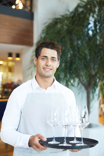 Portrait of smiling young waiter carrying empty wineglasses at the restaurant