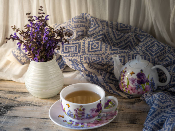 Bouquet of mauve flowers in a vase and blue fabric on rustic wooden table, with a white curtain background