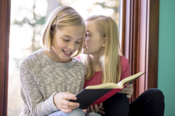 istock Sisters reading a book together in a window seat 1058250460