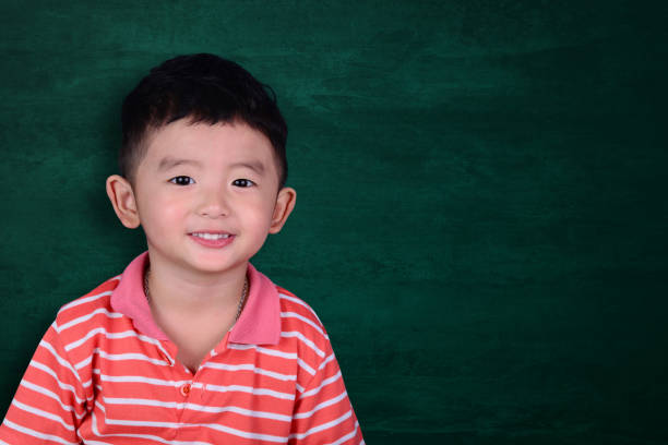 istock Happy Asian kid smiling on empty green chalkboard with copy space for add text or word, education and back to school concept. 1058259430