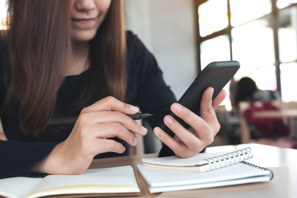 istock Closeup image of an Asian woman holding , using and looking at smart phone while working and writing 1058262508