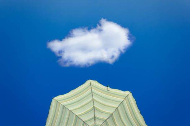 Yellow striped parasol against bright blue sky with one lonely white cloud