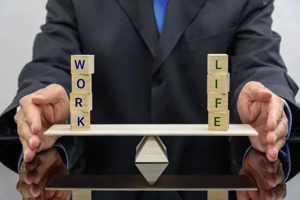 Work life balance concept : Businessman uses his hand protects 2 words on a seesaw or basic balance scale, depicts the balancing between time allocated for work and other aspect of life e.g family etc