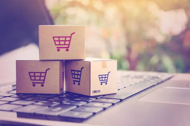 Photo of Online shopping / ecommerce and delivery service concept : Paper cartons with a shopping cart or trolley logo on a laptop keyboard, depicts customers order things from retailer sites via the internet.