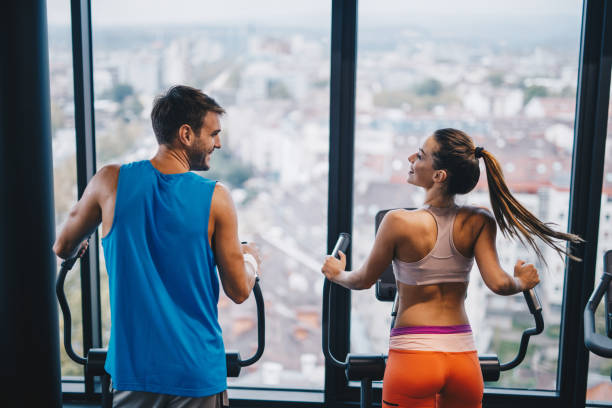 vue arrière du souriant sport couple parler pendant l’exercice dans une salle de gym. - cross trainer photos et images de collection