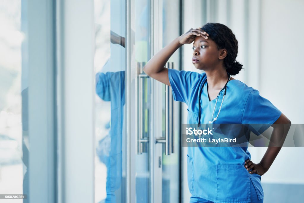 Doctors face heavy levels of stress too Shot of a young female nurse looking stressed out while standing at a window in a hospital Nurse Stock Photo