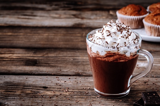 Hot chocolate drink with whipped cream in a glass on a wooden rustic background
