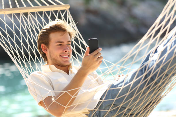 istock Happy man resting on a hammock using a smart phone 1058294558