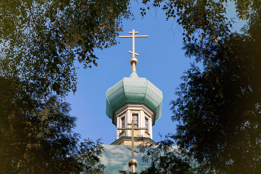 Dome of the old Orthodox church with a cross through the foliage of trees against blue sky. A symbol of the Church of Jesus Christ. Faith concept