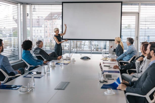 istock Mature CEO giving a business presentation through projection screen in a board room. 1058308290