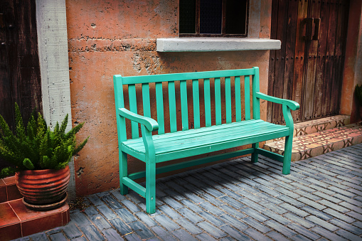 A green bench rests on the sidewalk. By the wall