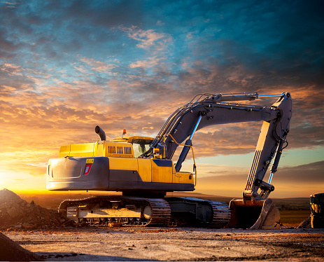 Excavator at a construction site against the setting sun. Excavator on the background of the setting sun. Huge excavator in the evening. Tracked excavator at the construction site in the evening.