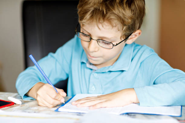 istock Cute little kid boy with glasses at home making homework, writing letters and doing maths with colorful pens. Little child doing exercise, indoors. Elementary school and education, imagine fantasy concept 1058331164