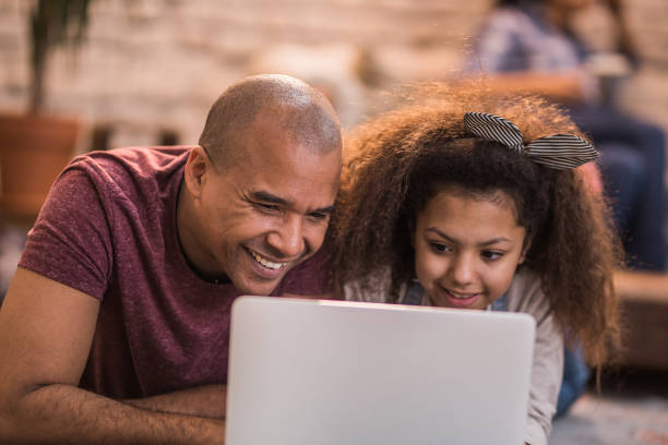 istock Happy black father and his daughter relaxing at home and using laptop. 1058332414