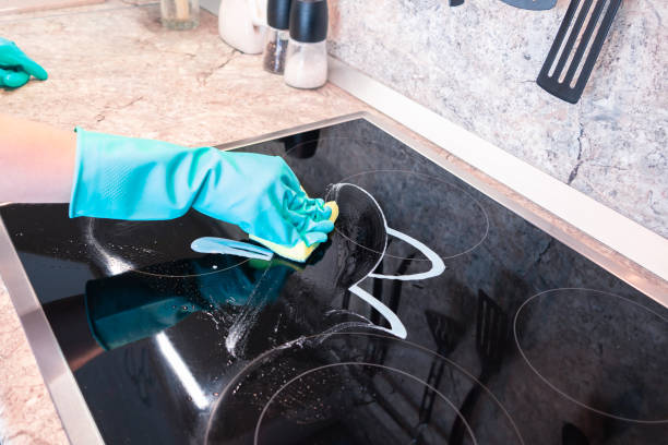 istock Woman's hand in a glove cleans a black cooker panel 1058333142