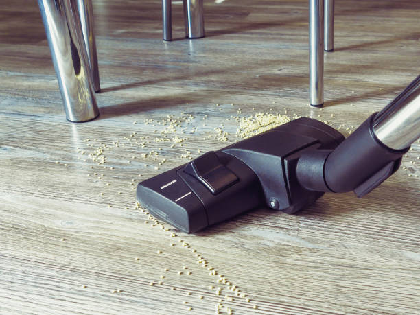 istock Garbage on the floor is cleaned with a vacuum cleaner. In the frame, a brush from a vacuum cleaner, legs of tables and chairs, a floor with a pattern for wood 1058333570