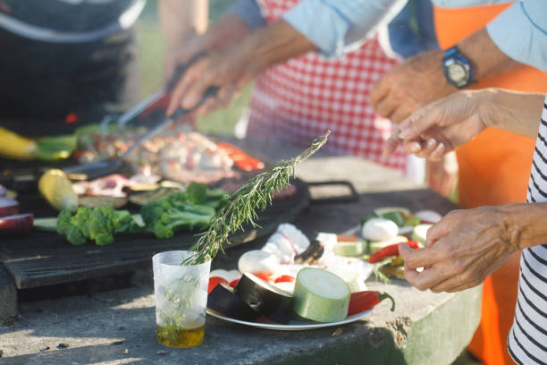 A close-up of active senior people barbecuing food and having a great time outdoors during a picnic day.