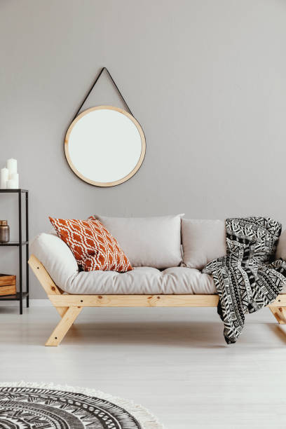istock Mockup of round mirror above grey settee with patterned blanket in boho flat interior. Real photo 1058343786
