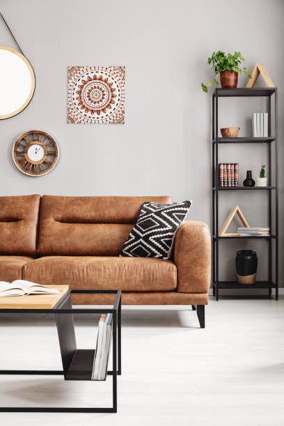 istock Patterned pillow on leather couch in grey ethno apartment interior with table and poster. Real photo 1058343788