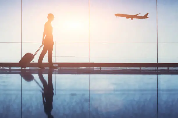 Photo of Travel. Silhouette of woman passenger with baggage in airport.