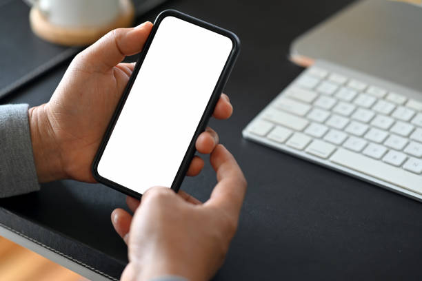 istock Man's hand holding white screen mobile phone on desk in office 1058354342
