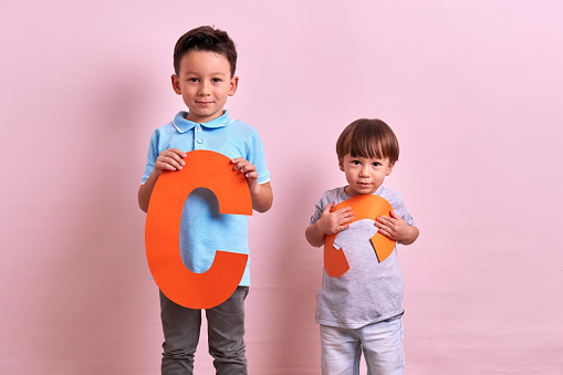 Studio portrait of kids with cutout letters on pink background