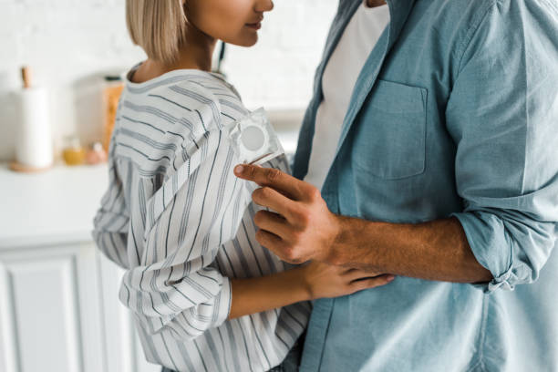 cropped image of boyfriend hugging girlfriend and holding condom in kitchen cropped image of boyfriend hugging girlfriend and holding condom in kitchen condom photos stock pictures, royalty-free photos & images