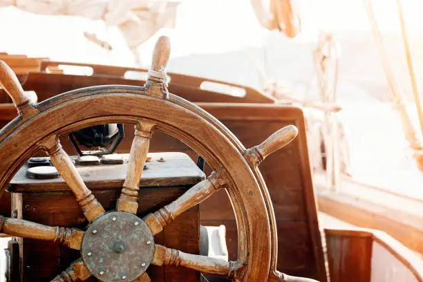 Closeup of a vintage hand wheel on a wooden sailing yacht. Yachting, helm of old wooden sailboat in port of sailing, rope, steering wheel, details of yacht.