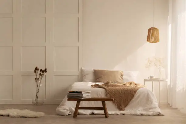 Beige blanket on the double bed in stylish wabi sabi bedroom of minimal style house, real photo with copy space on the empty wall