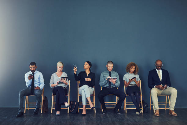 Now comes the wait Studio shot of a group of businesspeople using wireless devices while waiting in line people in a row photos stock pictures, royalty-free photos & images