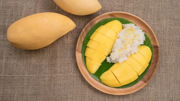 Thai style dessert, mango with glutinious rice on burlap background