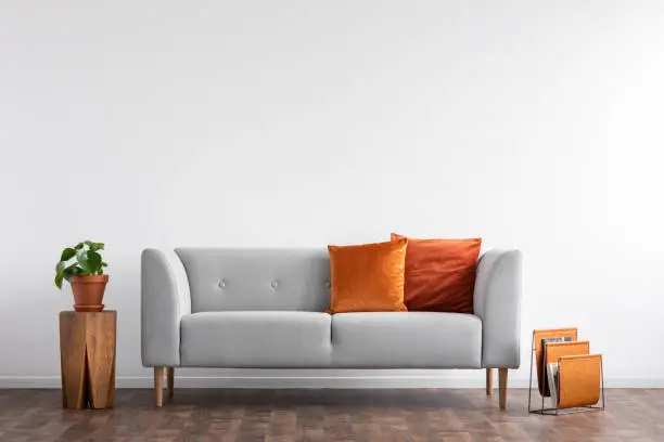 Photo of Comfortable couch with orange and red pillow in spacious living room interior, real photo with copy space on the empty white wall