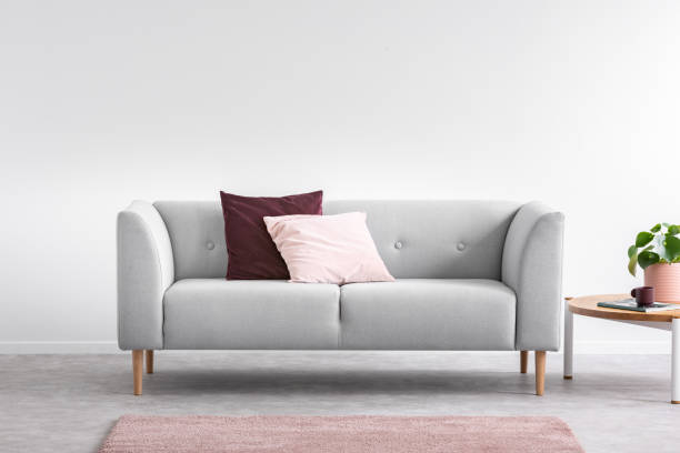 almofada rosa roxa e pastel no confortável sofá cinza brilhante sala interior com tapete rosa e mesa de café, foto real com espaço de cópia na parede branca vazia - bedding cushion purple pillow - fotografias e filmes do acervo