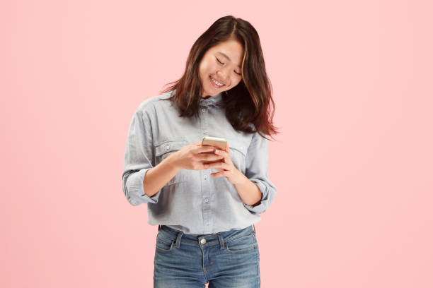 istock Young beautiful woman using mobile phone studio on pink color background 1058372246
