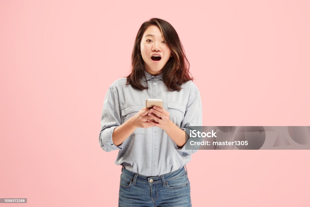 Young beautiful woman using mobile phone studio on pink color background Young beautiful woman using mobile phone studio on pink color studio background. Human facial emotions concept. Trendy colors Asian and Indian Ethnicities Stock Photo