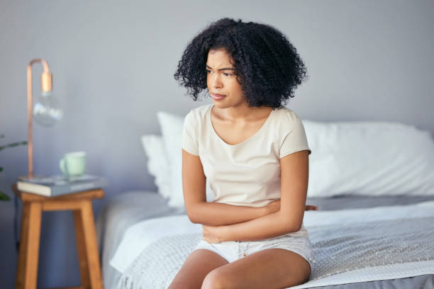 She's a little under the weather Shot of a young woman suffering from stomach cramps in her bedroom uncomfortable stock pictures, royalty-free photos & images