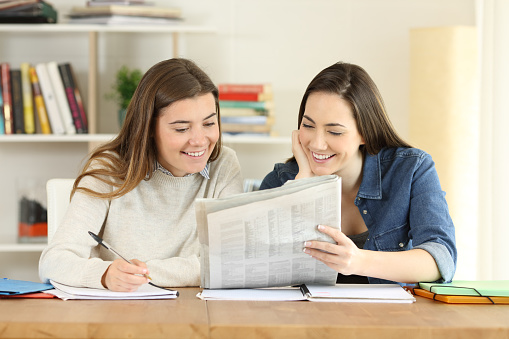 Two happy students talking about newspaper news at home