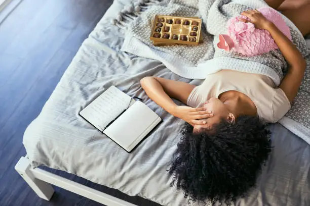 Shot of a young woman suffering from menstrual cramps in her bedroom