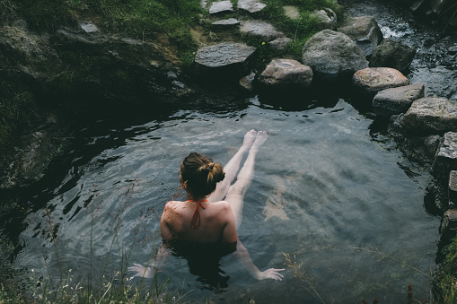 Woman in red swimsuit chillin in beautiful natural hot pool on Westfjords in Iceland